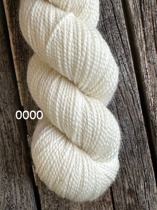 A skein of white KPM and KPPPM Variegated Color Collection yarn, color 0000, rests on weathered wooden planks—perfect for your next hand knitting project.