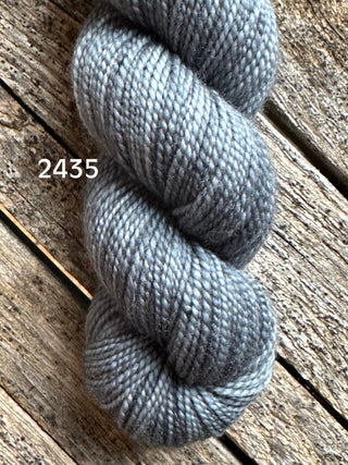 A close-up of Koigu KPM & KPPPM Fingering Weight Yarn in color 2435, tightly twisted and soft with a smooth, subtle sheen, resting on a rustic wooden surface.