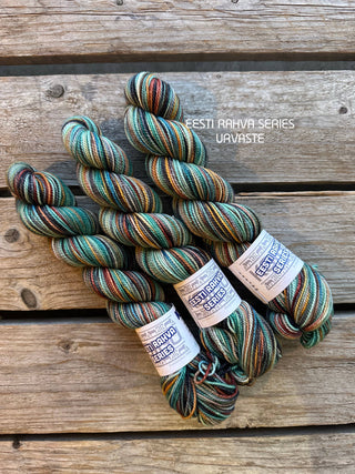 Three skeins of Eesti Rahva (Estonian Folk) Series 2025 - KPPPM yarn in the URVASTE colorway rest on a rustic wooden surface—ideal for Estonian handicrafts or folk costume knitting projects.