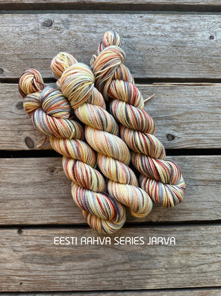 Four skeins of KPPPM Merino wool yarn in yellow, orange, brown, and gray (color: JARVA) from the Eesti Rahva (Estonian Folk) Series 2025 are displayed on a wooden surface.