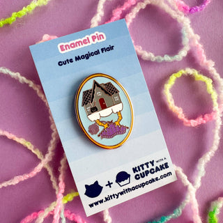 Add the Baba Yaga Knitting Enamel Pin to your collection—an adorable enamel pin of a chicken-legged house, displayed on a blue-striped card that reads “Enamel Pin, Cute Magical Flair,” set against a pink background with colorful yarn loops.