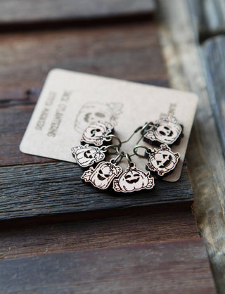 🎃 Pumpkin Jack O’Lantern Stitch Markers are shown on a brown card atop a rustic wooden surface, featuring pumpkin designs.