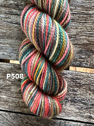 A skein of KPM and KPPPM Variegated Color Collection yarn in shade P508 (pink, green, yellow, brown) rests on a rustic wooden surface—perfect for hand knitting projects.