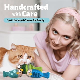 A woman in a pink shirt and headband smiles at an orange and white cat playing with Felted Fish Cat Toys. Text reads, “Handcrafted with Care—Just Like You’d Choose for Family.”.
