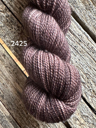 A skein of Koigu KPM & KPPPM Fingering Weight Yarn in soft brownish-purple (color 2425) with a smooth, slightly shiny, tightly twisted texture rests on rustic wood—ideal for knitting or crochet projects.