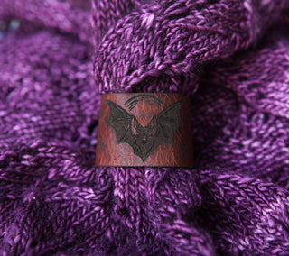 The 🦇 Vampire Bat Under the Moon Shawl Cuff 🦇 is a brown handcrafted leather accessory with a black bat engraving, shown on textured purple knit—perfect for adding unique style to your knit or crochet projects.