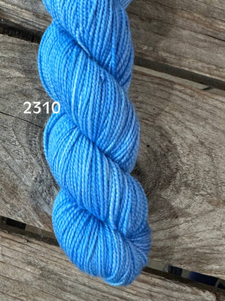 A skein of Koigu KPM & KPPPM Fingering Weight Yarn in bright blue, labeled 2310, is displayed on a rustic wooden surface.