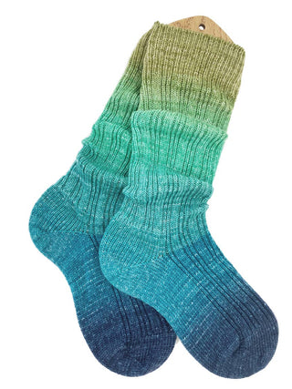 These cozy socks, knit with Solemate Sock Yarn, feature a gradient from dark blue toes to green and light brownish-olive tops, and are displayed on a wooden sock blocker.