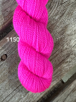The Koigu KPM & KPPPM Fingering Weight Yarn in color 1150, a bright pink skein, is displayed on a rustic wooden background—ideal for your next knitting or crochet project.