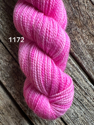 A pink skein from the KPM and KPPPM Variegated Color Collection Skeins, showing various shades, rests coiled on a rustic wooden surface. The number 1172 is displayed in white text on the yarn, perfect for hand knitting projects.