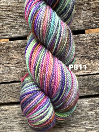 A skein from the KPM and KPPPM Variegated Color Collection features purple, pink, green, and blue hues on a rustic wood background. "P811" appears on the right—ideal for your next hand knitting project.