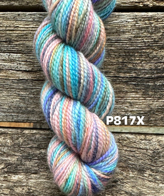 A skein from the KPM and KPPPM Variegated Color Collection in blue, pink, purple, and beige is twisted on a rustic wooden background. Ideal for hand knitting projects. The code P817X appears on the right of the image.
