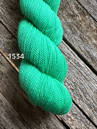 A skein of Koigu KPM & KPPPM Fingering Weight Yarn in bright turquoise, labeled 1534, sits on a weathered wooden surface.