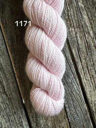 A skein of pale pink KPM and KPPPM Variegated Color Collection yarn, color 1171, rests on a rustic wooden surface—perfect for hand knitting projects.