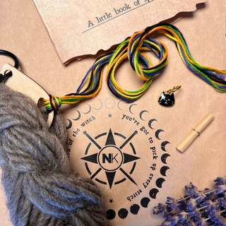 A Tatters the Cat Poppet | Family Knitting Kit containing a skein of gray yarn, multi-colored thread, a small black cat stitch marker, a paper scroll, and a sprig of dried lavender resting on a printed moon-phase project card.