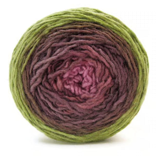 The Freia Ombre & Gradient Sport Wool Yarn is a hand-dyed cake featuring an ombre gradient from green on the outer edge to brown, purple, and pink at the center, shown against a white background.
