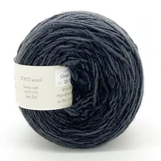 A ball of Freia Semi-Solid Sport Wool Yarn in dark gray, heavy sport weight, made from 100% US Columbia Corriedale Rambouillet wool. It features a white label with fiber content and care details. The yarn is soft and slightly textured.