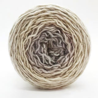 A close-up of a Freia Ombre & Gradient Sport Wool Yarn ball, hand-dyed in beige, cream, and light brown tones, showcasing its soft, slightly uneven texture against a plain white background.