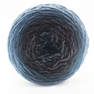 A close-up of a round skein of Freia Ombre & Gradient Sport Wool Yarn, featuring tightly wound strands that transition from dark blue at the center to lighter blue on the outer edges.
