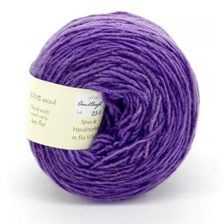 A ball of Freia Semi-Solid Sport Wool Yarn in purple features a white label with material and care info. Made from 100% US wool, this heavy sport weight yarn showcases a rich hue and a soft, textured appearance.