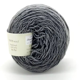 A ball of Freia Semi-Solid Sport Wool Yarn in gray, DK weight, with a white label featuring care and material details in fine print. The yarn looks soft and woolly, coiled neatly into a round shape.