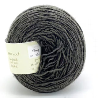 A ball of Freia Semi-Solid Sport Wool Yarn in Ebony, made of 100% US wool, features a dark gray color and soft, slightly fuzzy texture. The heavy sport weight yarn sits on a white background with a visible tag wrapped around it.