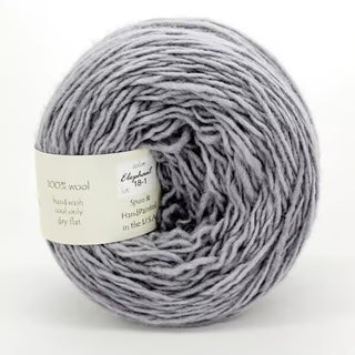 A close-up of Freia Semi-Solid Sport Wool Yarn in the “Elephant” color, a soft light gray DK weight yarn with a white label stating “100% US wool,” “hand wash,” and “Spun & Handpainted in the USA.”.