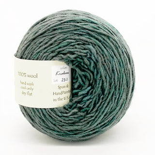 A ball of Freia Semi-Solid Sport Wool Yarn in Kraken (lot 23-1), grayish-green, 100% US Columbia Corriedale Rambouillet wool, hand wash cool only, dry flat, spun & handpainted in the USA.