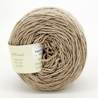 A ball of Freia Semi-Solid Sport Wool Yarn in light beige—100% US wool, DK weight—is neatly wound with a partially visible label displaying color, lot number, and care details.