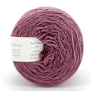 A ball of Freia Semi-Solid Sport Wool Yarn in soft rose-mauve, made from 100% US wool, neatly wound with a white label displaying product details. The sport weight yarn has a smooth, luxurious texture.