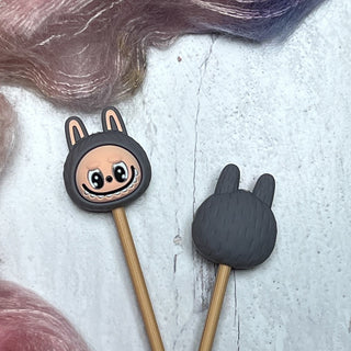 These gray Knitting Needle Stitch Stoppers are shaped like adorable bunny-eared creatures in polymer clay—one with a cheerful face, one showing the back—and come attached to sticks, ideal for keeping your stitches secure.