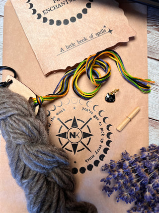 Tatters the Cat Poppet knitting kit including a hank of grey yarn, multicolored embroidery floss, a small cat-shaped charm, a scroll, and dried lavender, resting on a branded paper envelope.
