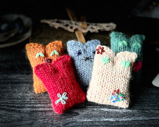 Five Tatters the Cat Poppet hand-knitted dolls in orange, red, blue, green, and cream, each decorated with embroidered faces or flower appliqués.