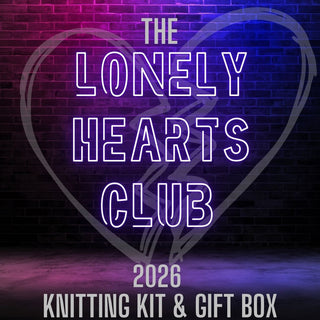 Neon text spells “Lonely Hearts Club KAL Kit” on a dark brick wall with a purple and pink broken heart outline, featuring Lazy Bee Yarn and soft Superwash Merino for the perfect Lonely Hearts Club knitting kit.