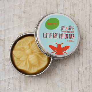 An open round tin of Little Bee Lotion Bar rests on a light wood surface, showcasing a bee-shaped yellow beeswax moisturizer with a lemongrass scent—ideal for deep hydration.