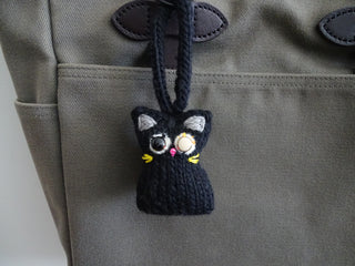 Small black Tatters the Cat Poppet with mismatched button eyes, hanging from a bag strap.