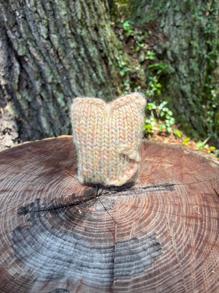 A small, hand-knitted Tatters the Cat Poppet in variegated pastel yarn sitting on a tree stump.