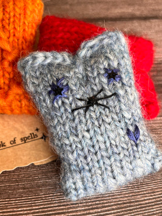 A small, rectangular, light blue Tatters the Cat Poppet knitting kit cat toy with dark blue embroidered eyes and whiskers.