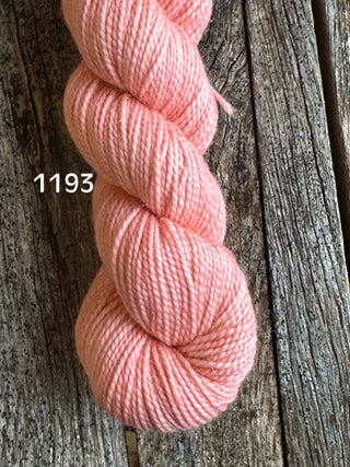 A skein from the KPM and KPPPM Variegated Color Collection in soft pink, color number 1193, rests on a rustic wooden surface—ideal for your next hand knitting project.