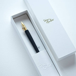 The One-Dip-Nib, a gold and black calligraphy pen with an adjustable nib, rests in a white textured box featuring Tonis Studio in gold on the lid—ideal for stunning line variation and displayed elegantly on a white surface.