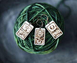 🔮 Tarot Card Stitch Markers – The Moon, The Star & The Sun 🔮: Three tarot card-themed earrings engraved with the Star, Sun, and Moon are shown on green-blue variegated yarn—perfect for marking stitches or tracking progress.