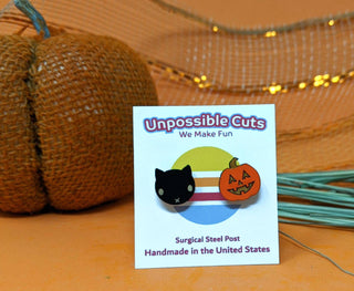 🐈‍⬛ Black Cat & Jack O’Lantern Earrings 🎃—a handmade pair on a Unpossible Cuts card, shown with a burlap pumpkin and autumn decor.