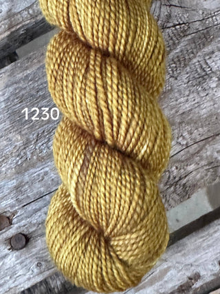 A skein from the KPM and KPPPM Variegated Color Collection in golden yellow, color 1230, rests on a rustic wooden surface—ideal for hand knitting projects.