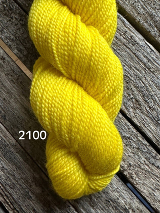 A skein of bright yellow yarn from the KPM and KPPPM Variegated Color Collection rests on a weathered wooden surface, showcasing its premium merino texture and vibrant color—ideal for hand knitting projects.