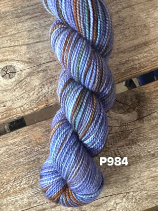 A skein from the KPM and KPPPM Variegated Color Collection in purple, blue, green, and brown rests on rustic wood. "P984" appears in white at the bottom right—perfect for hand knitting projects.