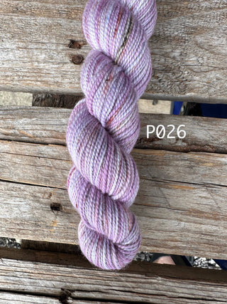 A skein of Bridgerton Collection KPPPM variegated light purple and white hand knitting yarn rests on a weathered wooden surface, with the label P026 visible in white text on the right side of the image.