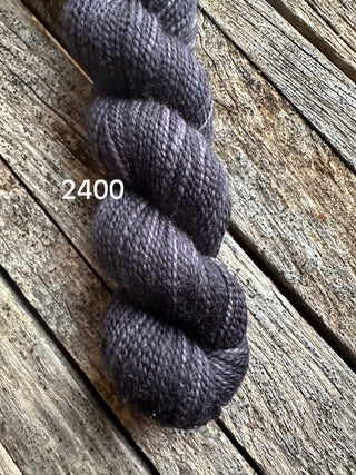 A skein of Koigu KPM & KPPPM Fingering Weight Yarn in color 2400 is displayed on rustic, weathered wooden boards.