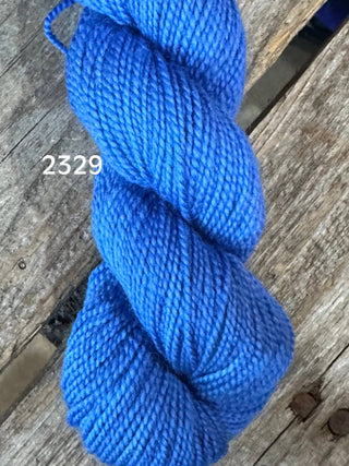 A skein of Koigu KPM & KPPPM Fingering Weight Yarn in bright blue, color 2329, sits on a weathered wooden surface.