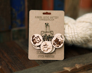 The 🐾 Scaredy Cats Stitch Marker Set features maple wood markers engraved with animal designs, attached to a Scarlet Knits card by Sunrise Grove Knittery. These unique knitting accessories are accented with yarn and rustic wood details.