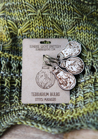 Three engraved wooden Terrarium Light Bulb Progress Keepers are attached to a card from Sunrise Grove Knittery, perfect for marking crochet or knitting progress, and displayed on green knit fabric.